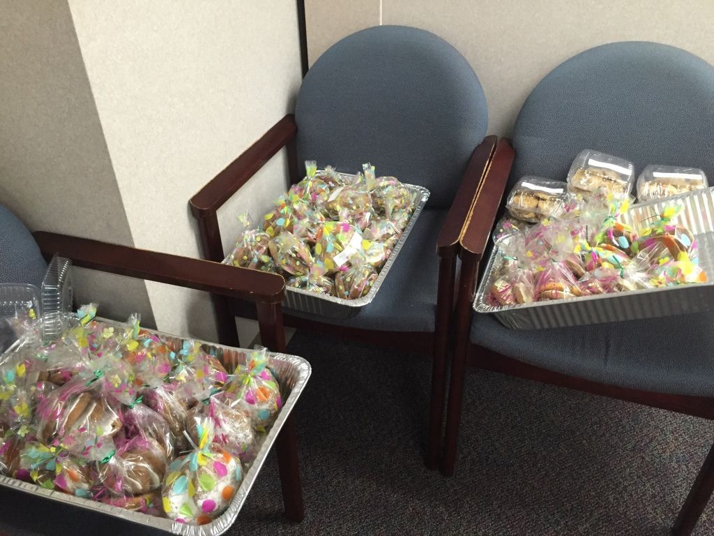 Three chairs are filled with trays of colorful cookies in clear, festive bags. 