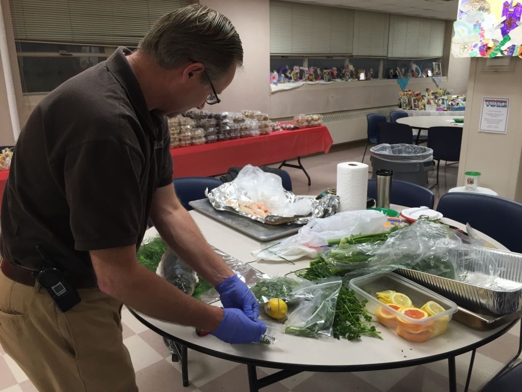 A man wearing a brown shirt and blue gloves prepares food at a table.