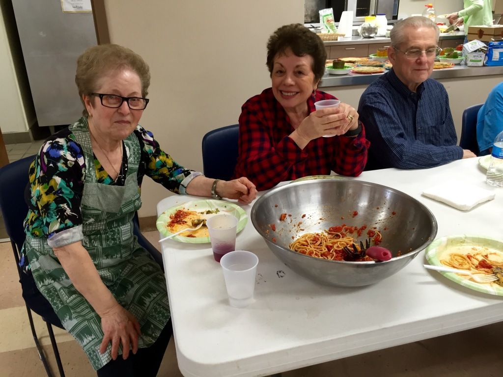 Three older adults sit at a table enjoying a meal.