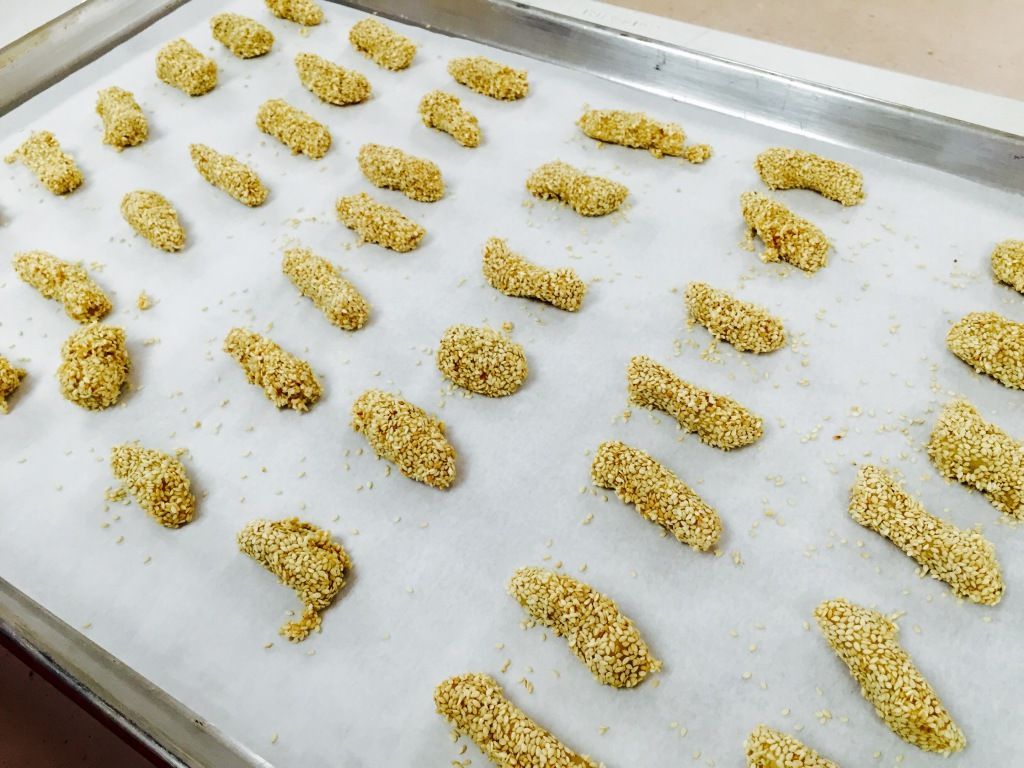 Baking sheet with evenly spaced, sesame-coated chicken fingers on parchment paper, ready for baking.