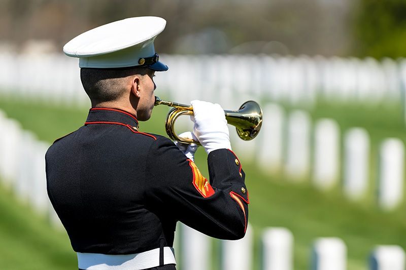 A man in a military uniform is playing a trumpet in front of a cemetery.