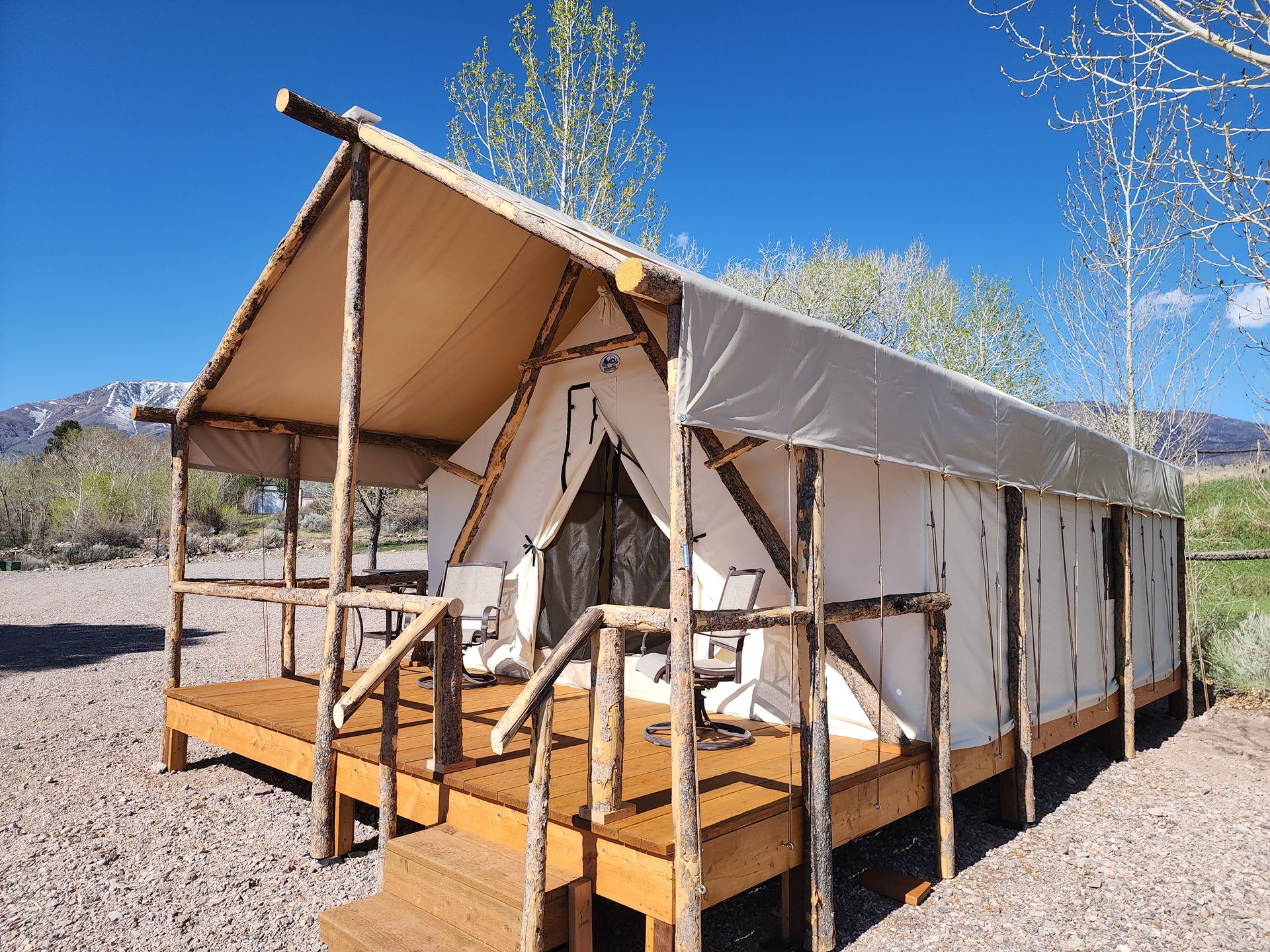 A safari-style glamping tent on a wooden deck in a rocky desert landscape with mountains in the background.