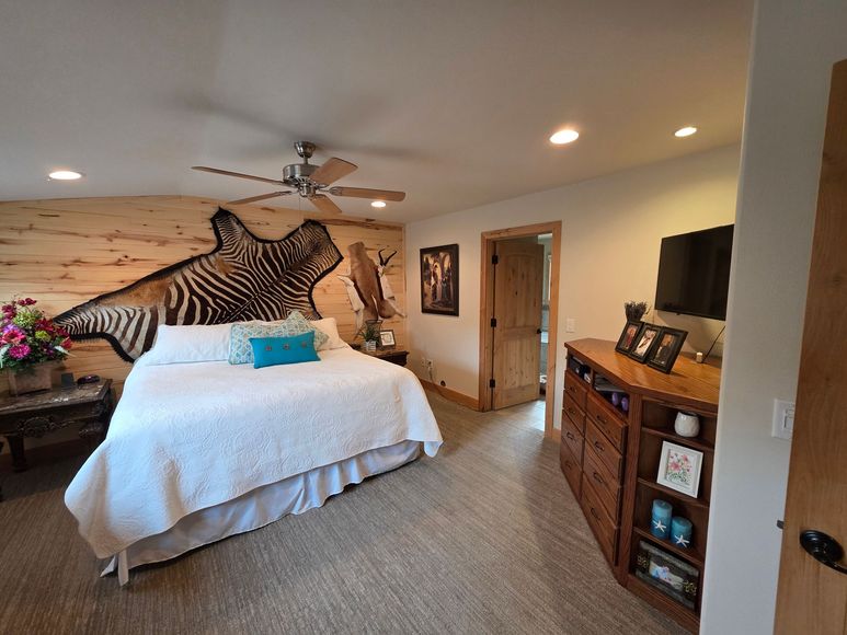 A bedroom featuring a large zebra-patterned headboard, a white bed, a wooden dresser with a TV, and a door to a hallway.