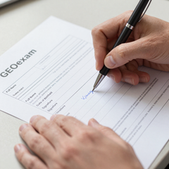 Una persona firmando un documento de GEOexam con un bolígrafo negro.