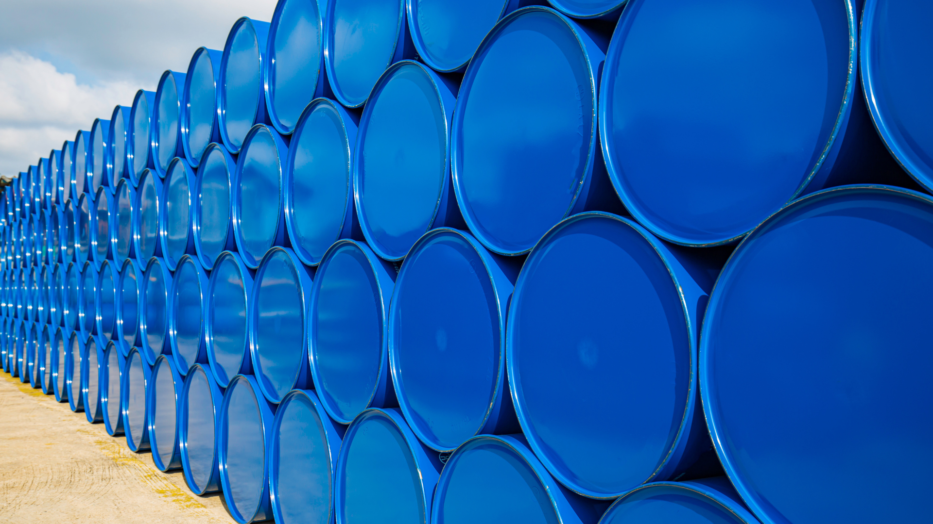Blue industrial barrels stacked in rows, outdoors.