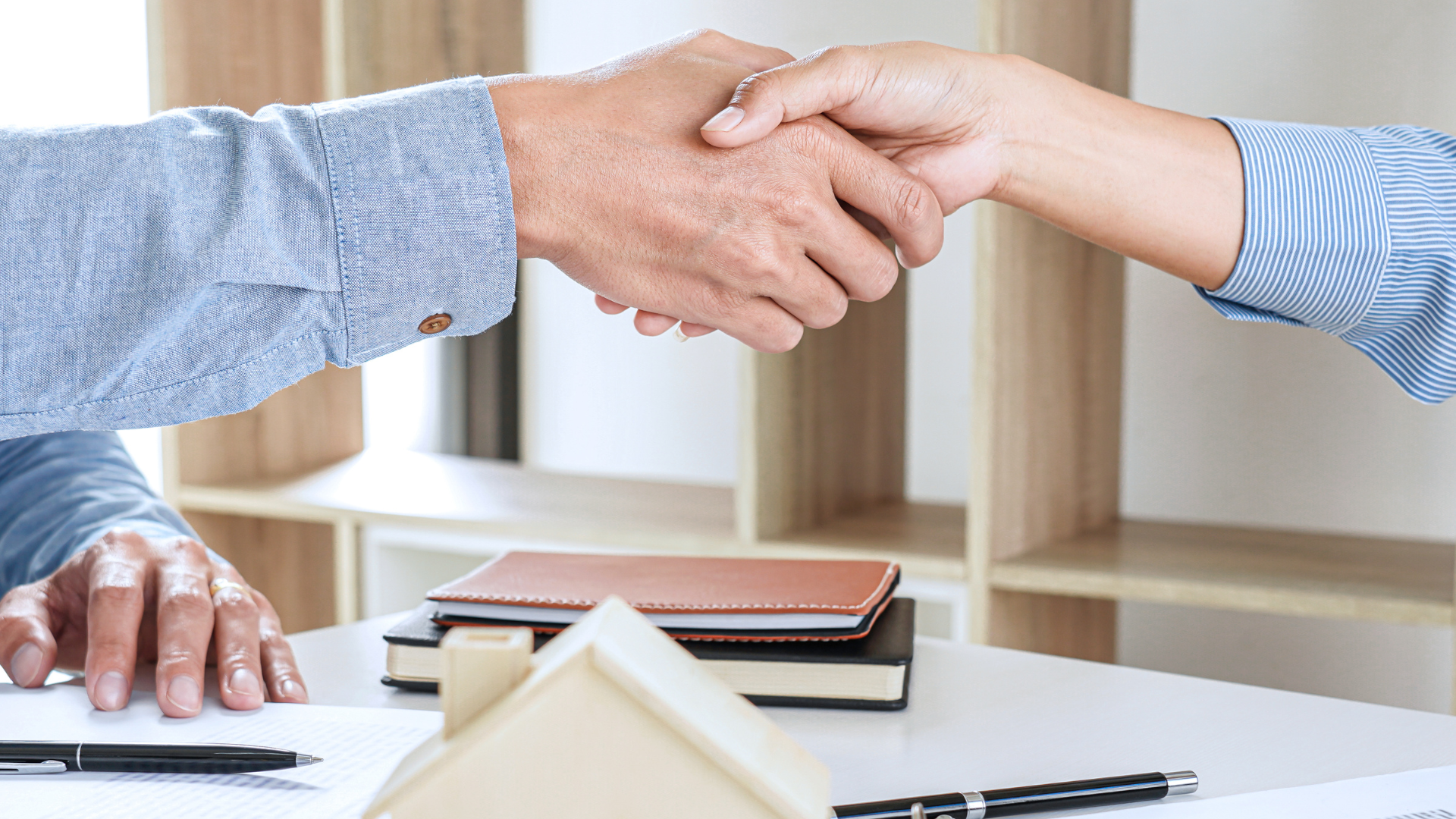 Two people shaking hands at a table; real estate deal.