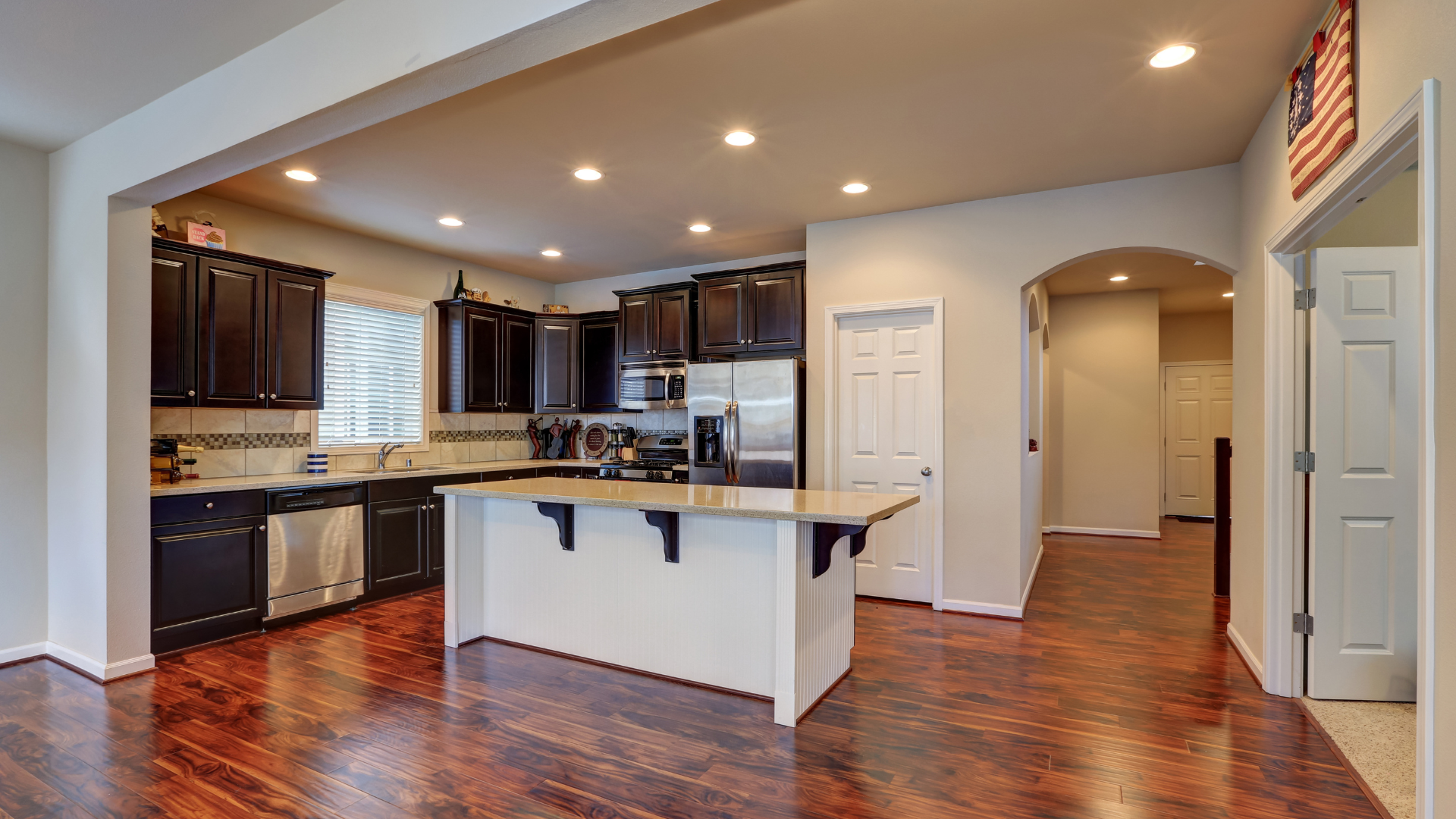 Kitchen with dark cabinets, island, stainless steel appliances, and wood floors.