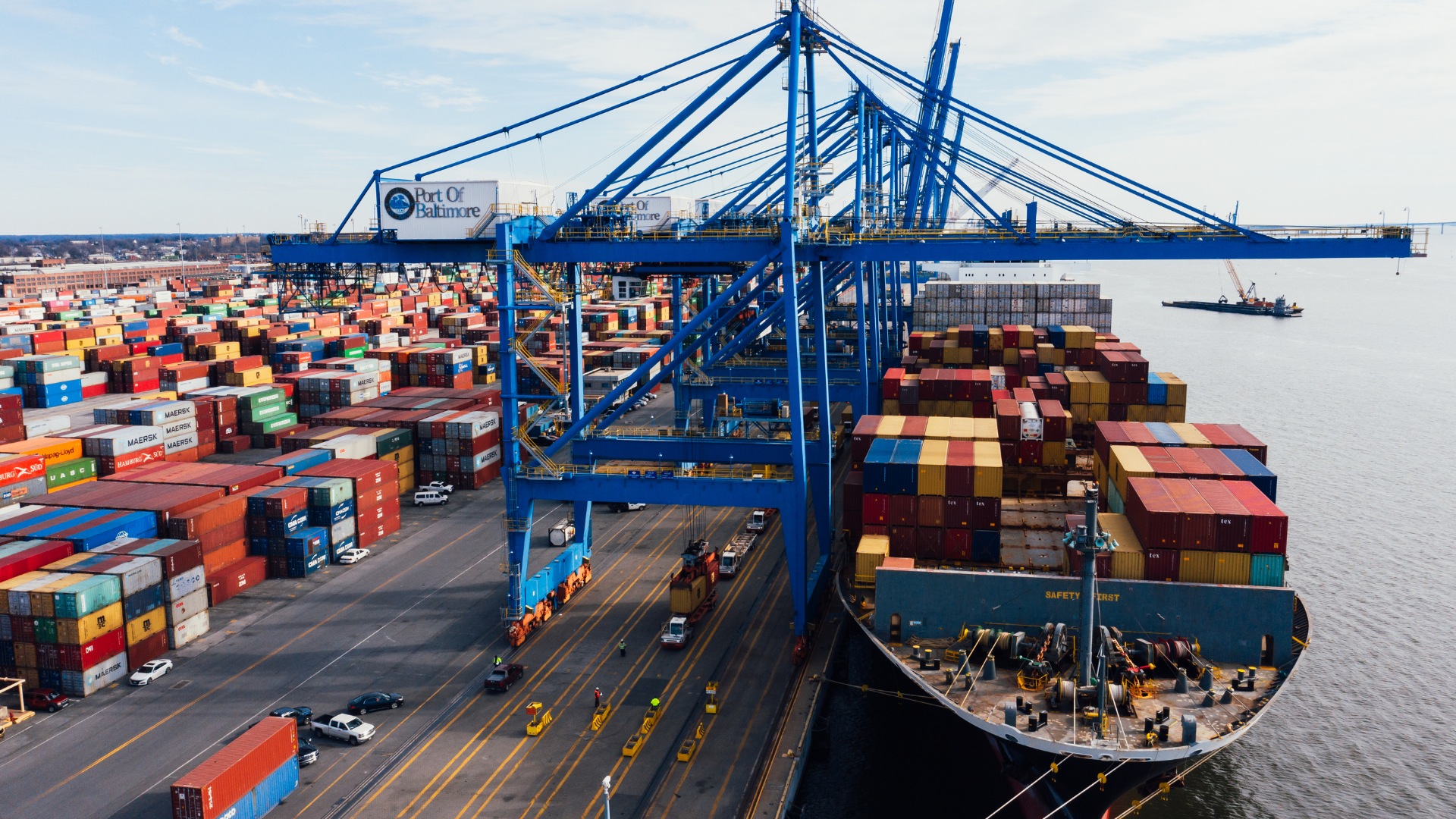 Cargo ship being unloaded at a port; blue cranes, colorful containers, sunny day.