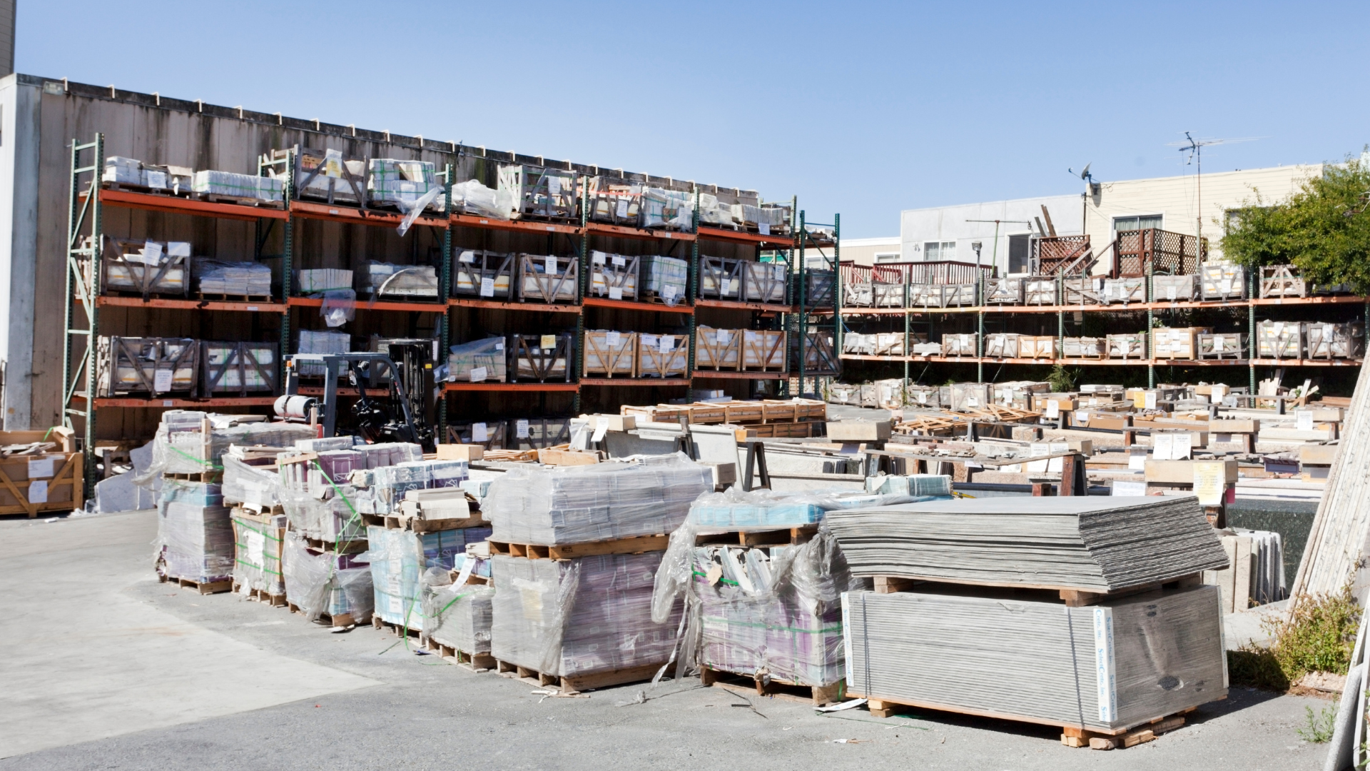Warehouse exterior with stacks of construction materials on shelves and pallets.