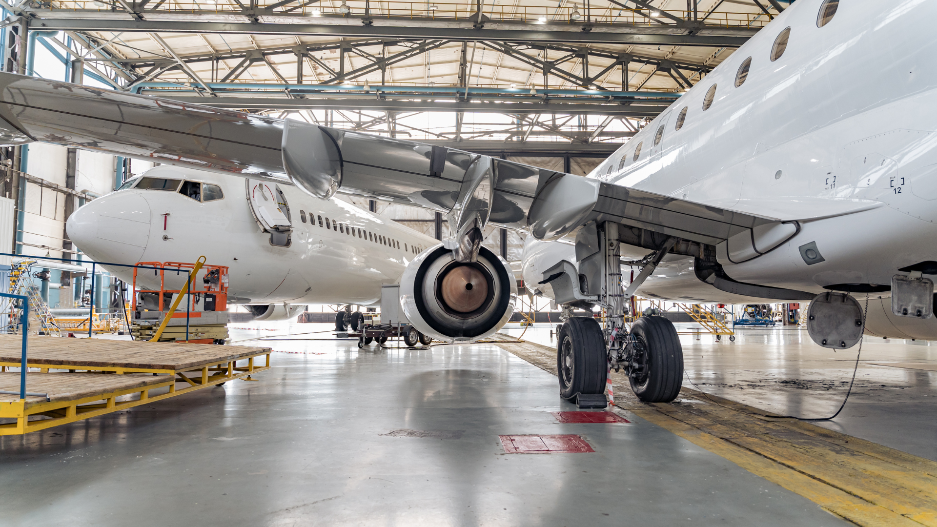 Two white airplanes in a hangar, one facing the camera. Landing gear and wings visible.