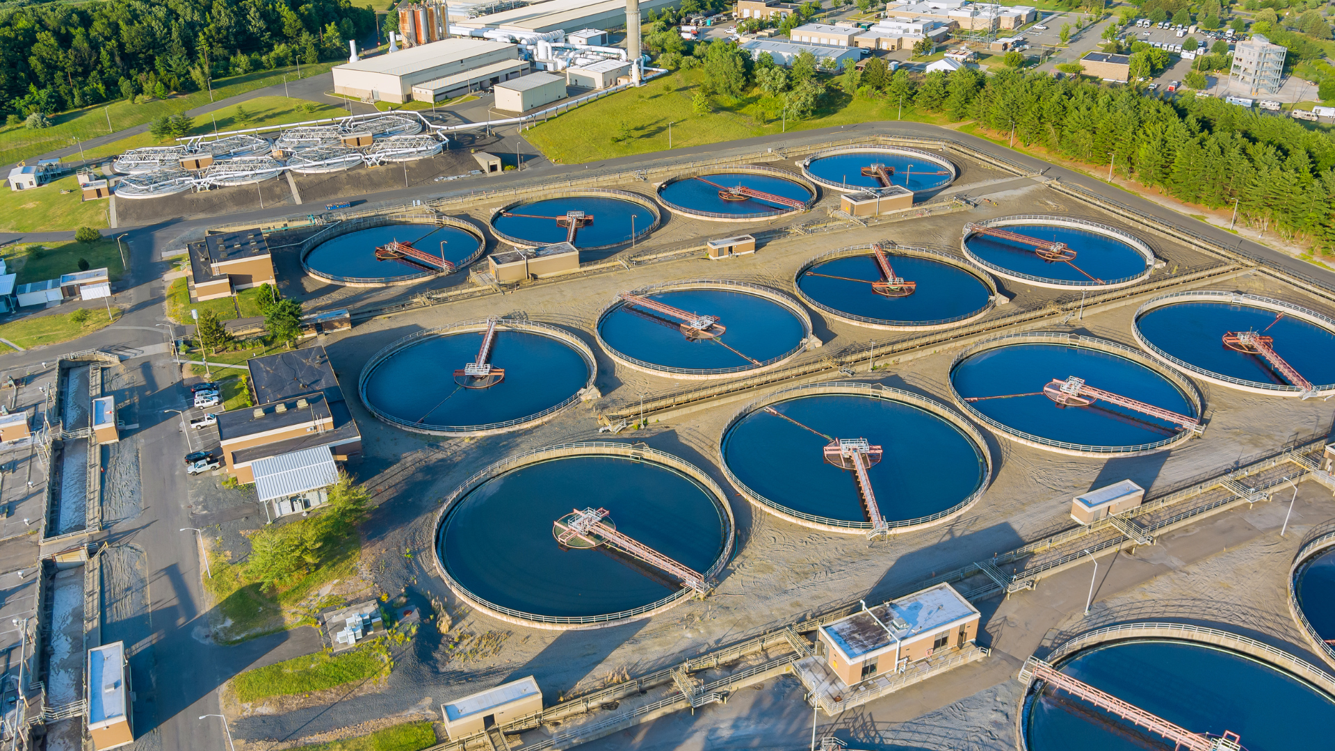 Aerial view of a wastewater treatment plant with several circular settling tanks filled with dark blue water.