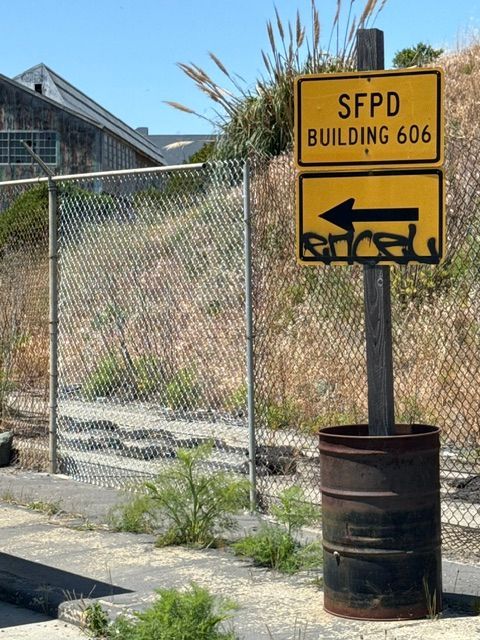 Sign for SFPD Building 606, with an arrow, post, and a rusty metal trash can.
