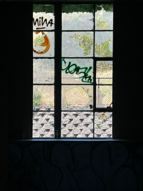 A rectangular window with graffiti, showing a courtyard. Dark interior, sunlight streams in.