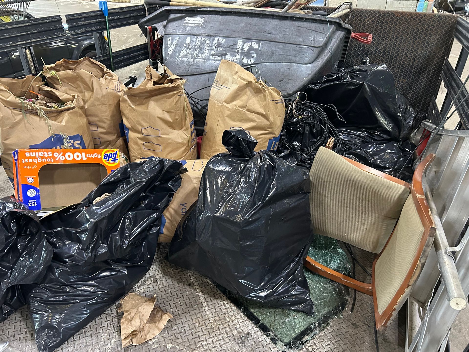 Bags of trash and debris piled in a dumpster, including black and brown paper bags.