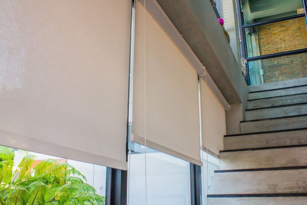 A Pair of Roller Blinds Hanging on a Window Next to a Set of Stairs — Port Blinds & Awnings In Coffs Harbour, NSW