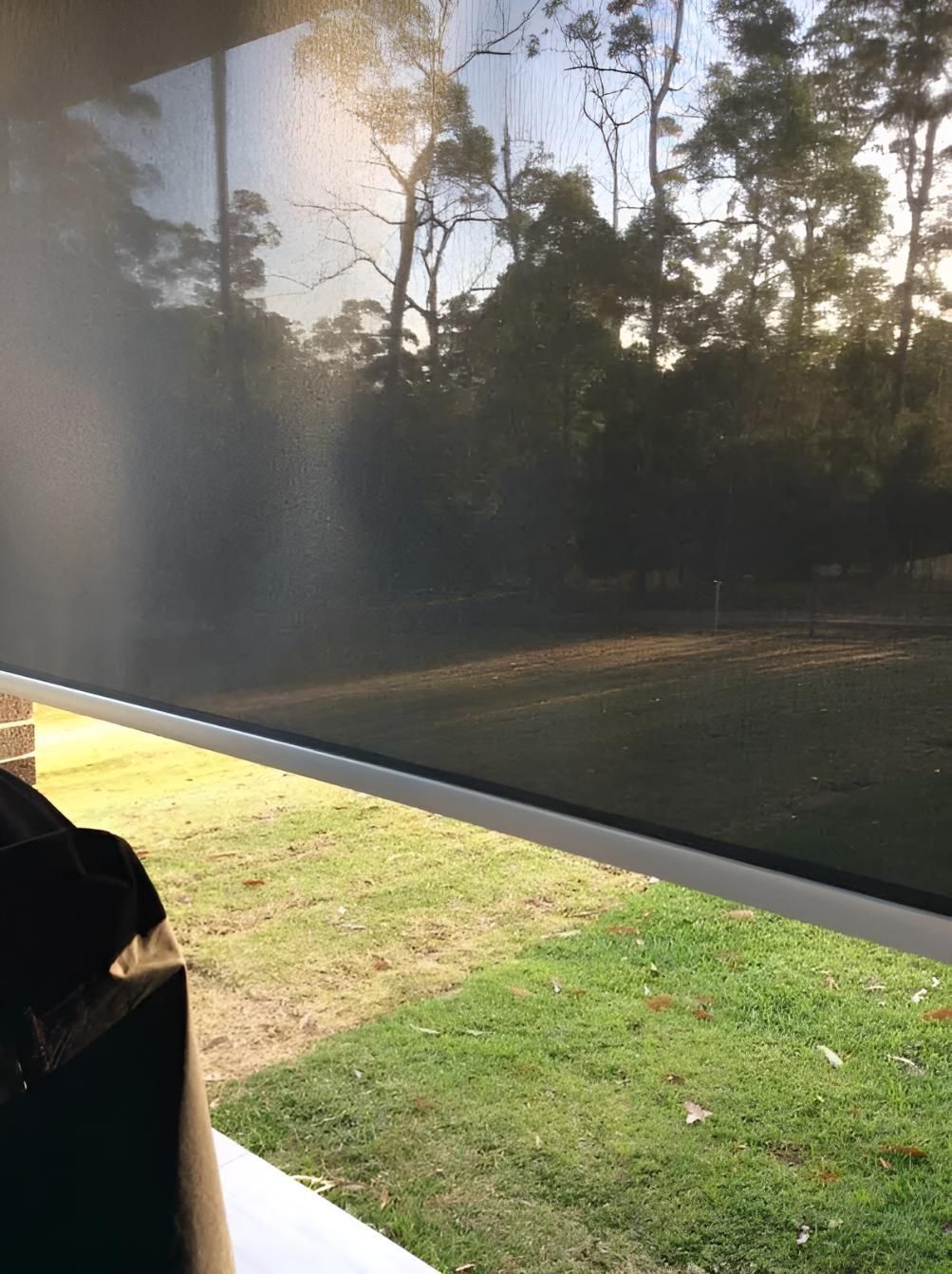 A Person is Sitting in Front of a Window With a Reflection of Trees in It — Port Blinds & Awnings In Port Macquarie, NSW
