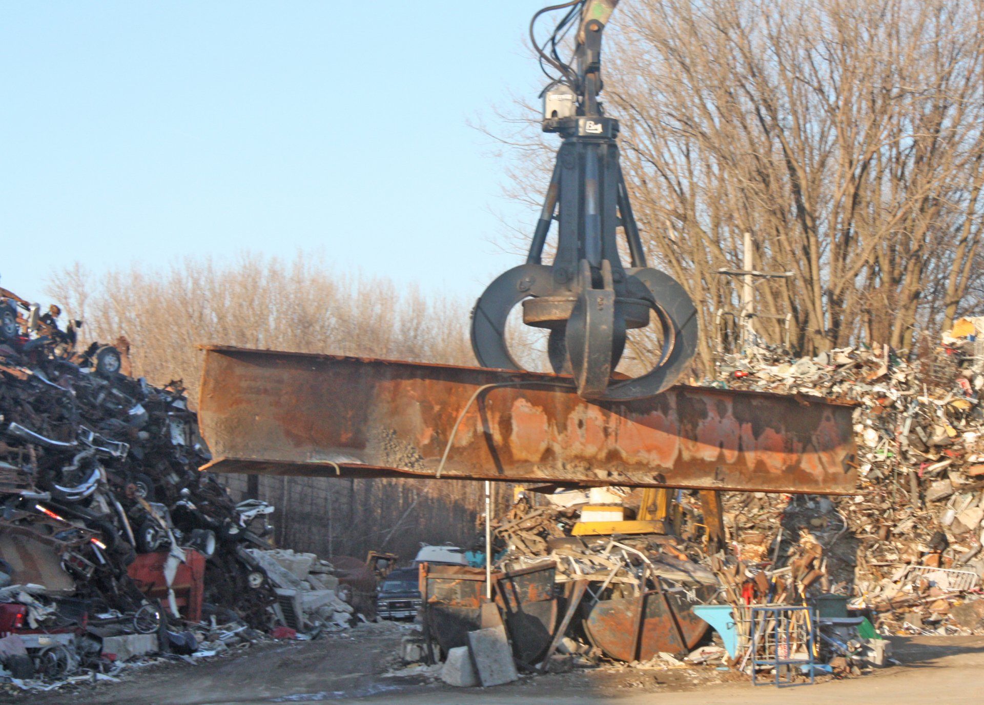 A crane is lifting a large piece of metal in a scrap yard.