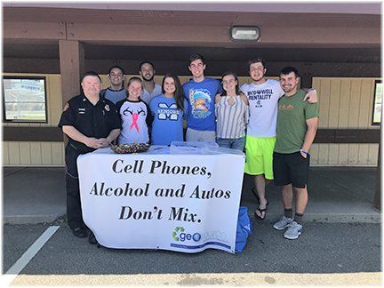 A group of people standing around a table that says cell phones alcohol and autos don 't mix.