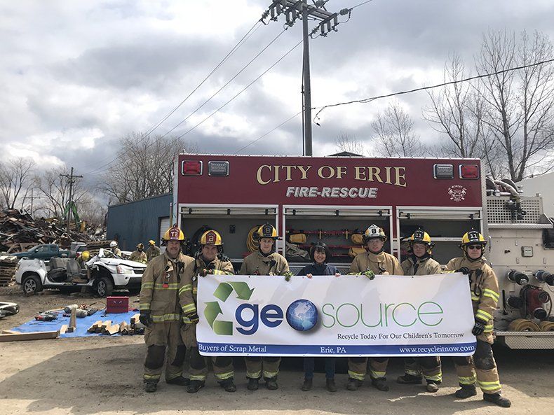 A group of firefighters holding a sign in front of a city of erie fire rescue truck.