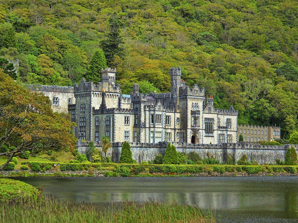 A large castle sitting on top of a hill next to a lake surrounded by trees.