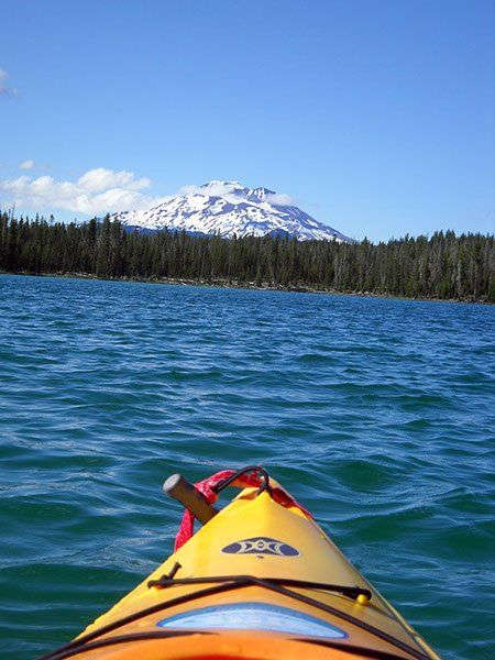 A yellow kayak is floating on a lake with a mountain in the background