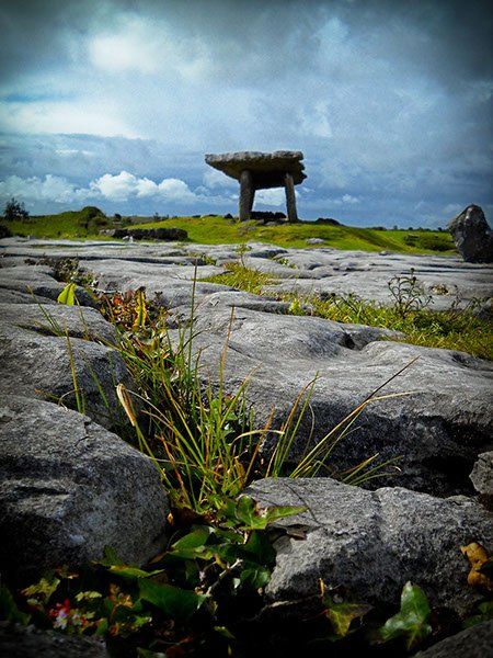 A stone structure is sitting on top of a grassy hill surrounded by rocks.