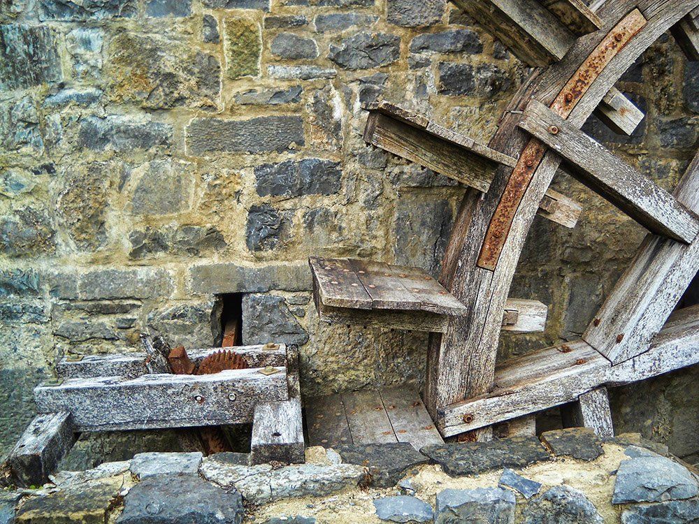 A wooden water wheel is sitting in front of a stone wall.