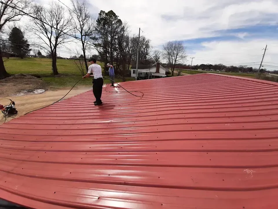 A man is cleaning a red metal roof with a broom.