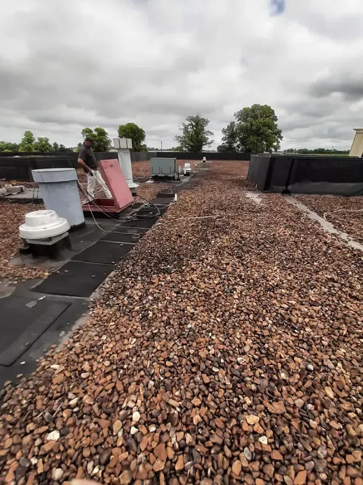 A man is standing on a roof with gravel on it.