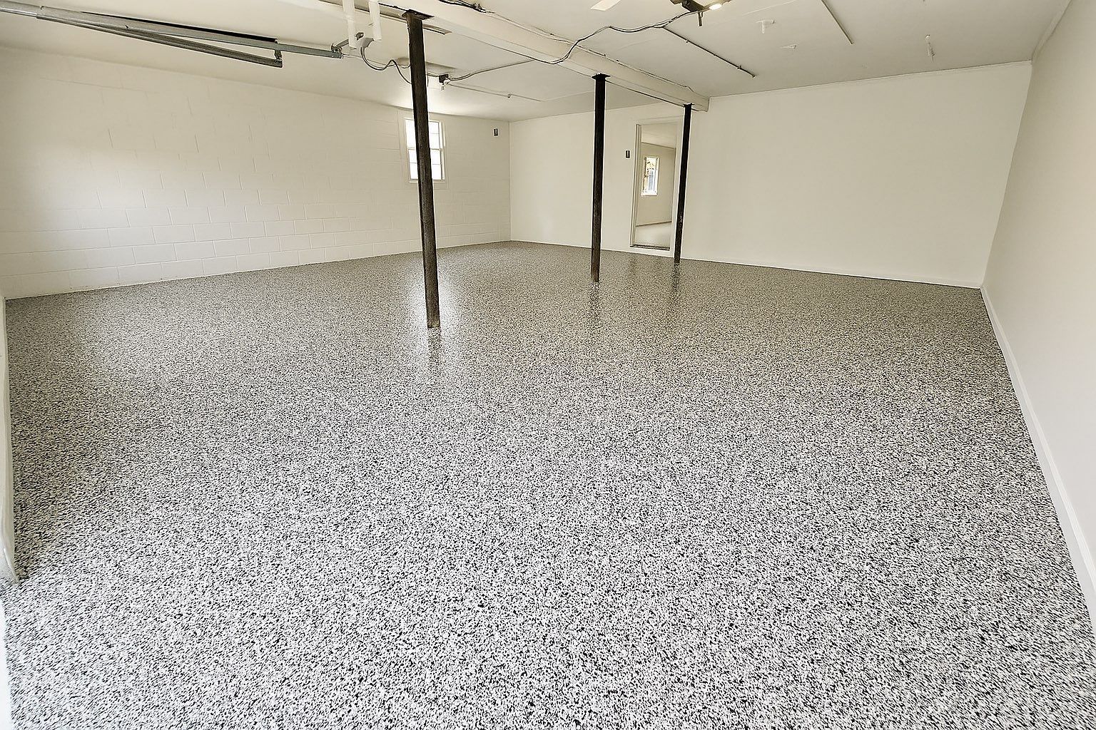 Garage with speckled gray and white epoxy floor, white walls, support beams, and open doorway.