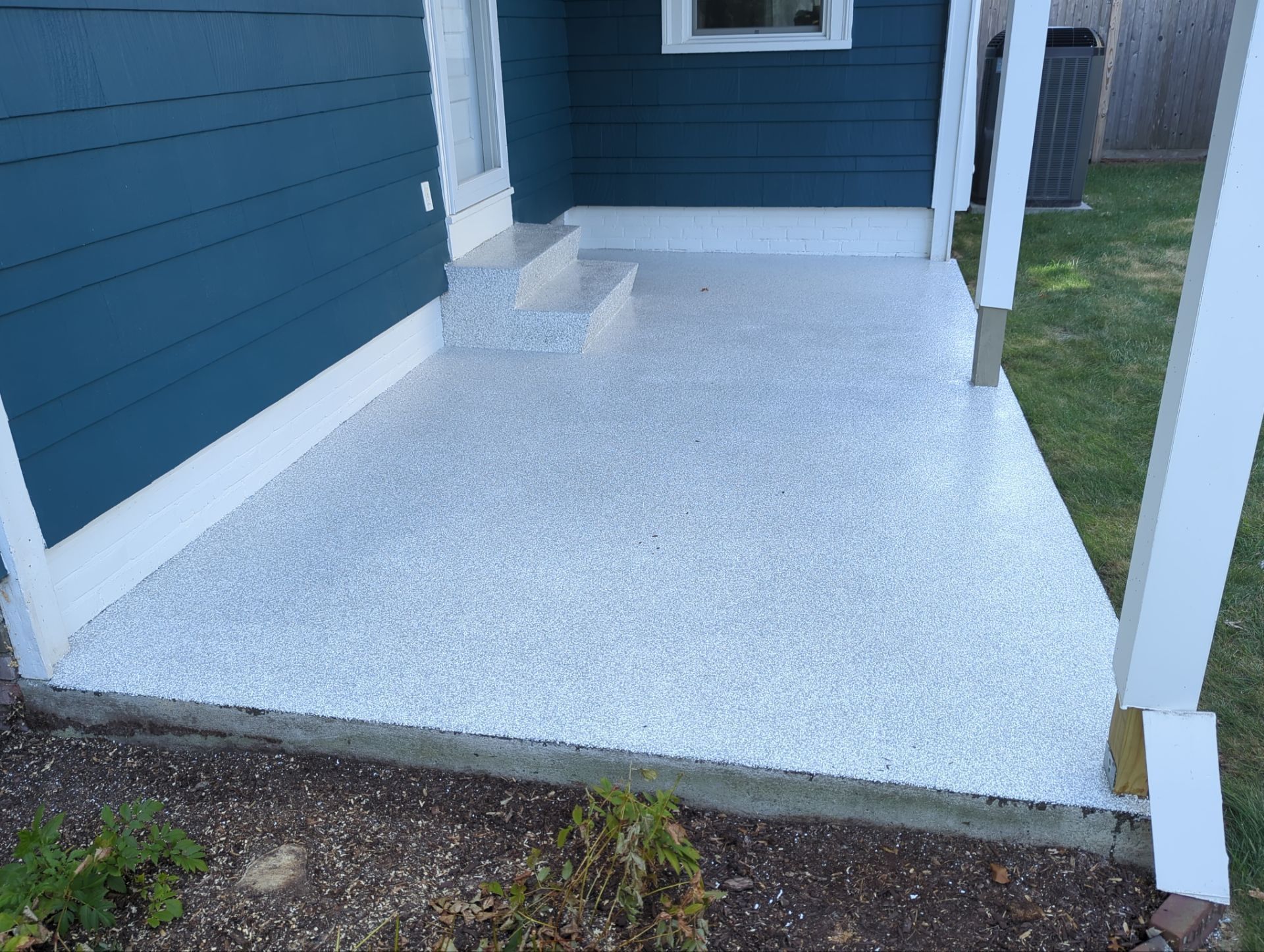 Exterior view of a concrete patio coated with white epoxy, adjacent to a blue house with white trim.