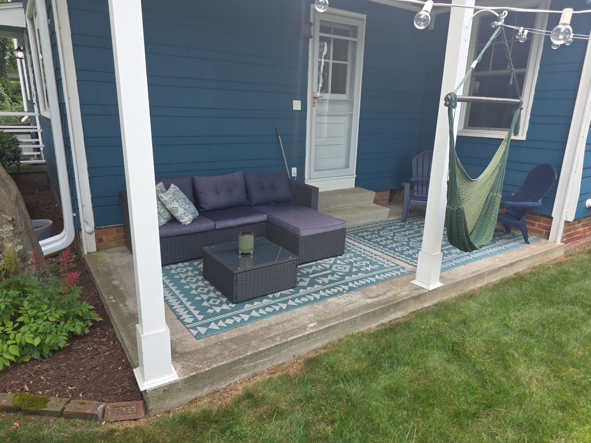 Patio with blue house, gray couch, teal rug, green hammock, and lawn.