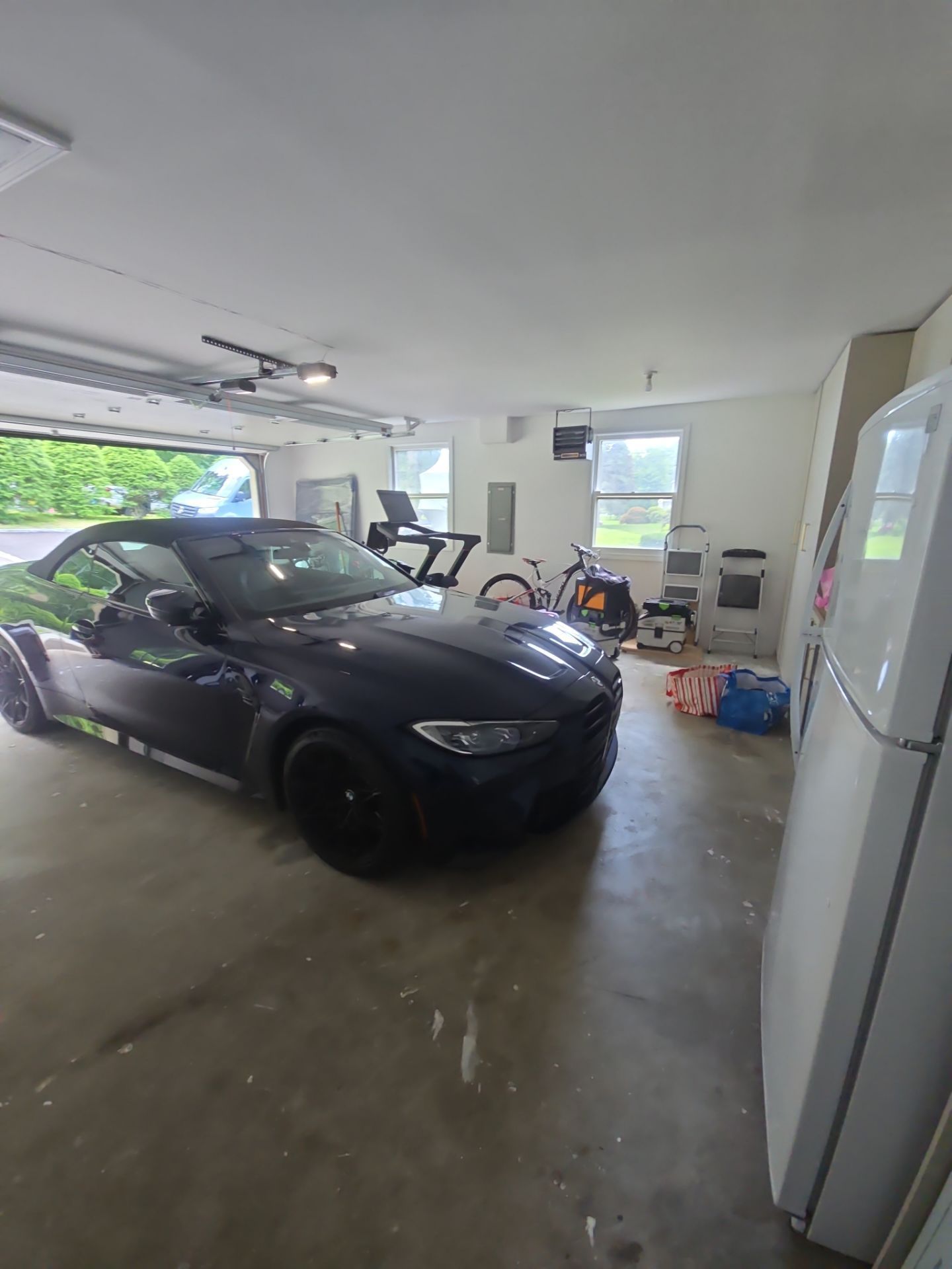 A dark blue convertible car is parked in a garage, with a treadmill and bike in the background.