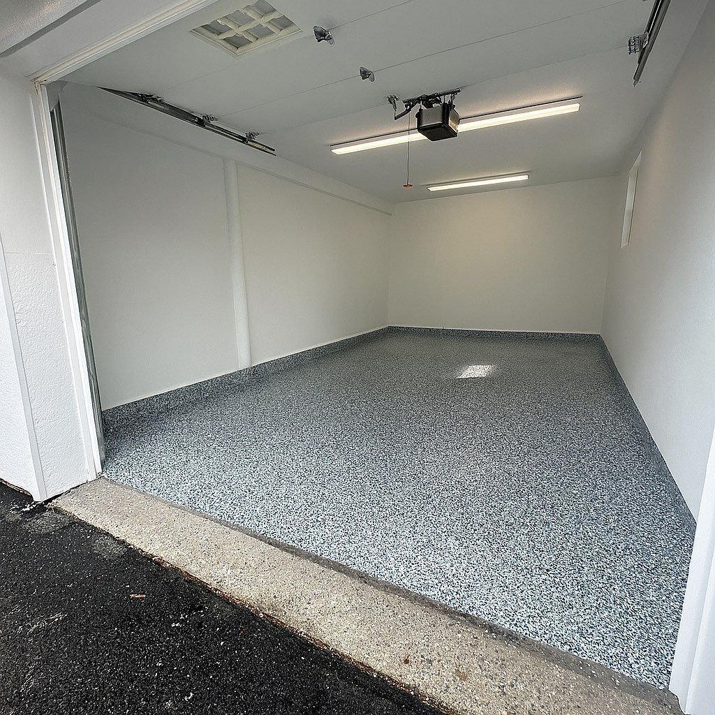 Empty garage with epoxy speckled floor, bright lighting.