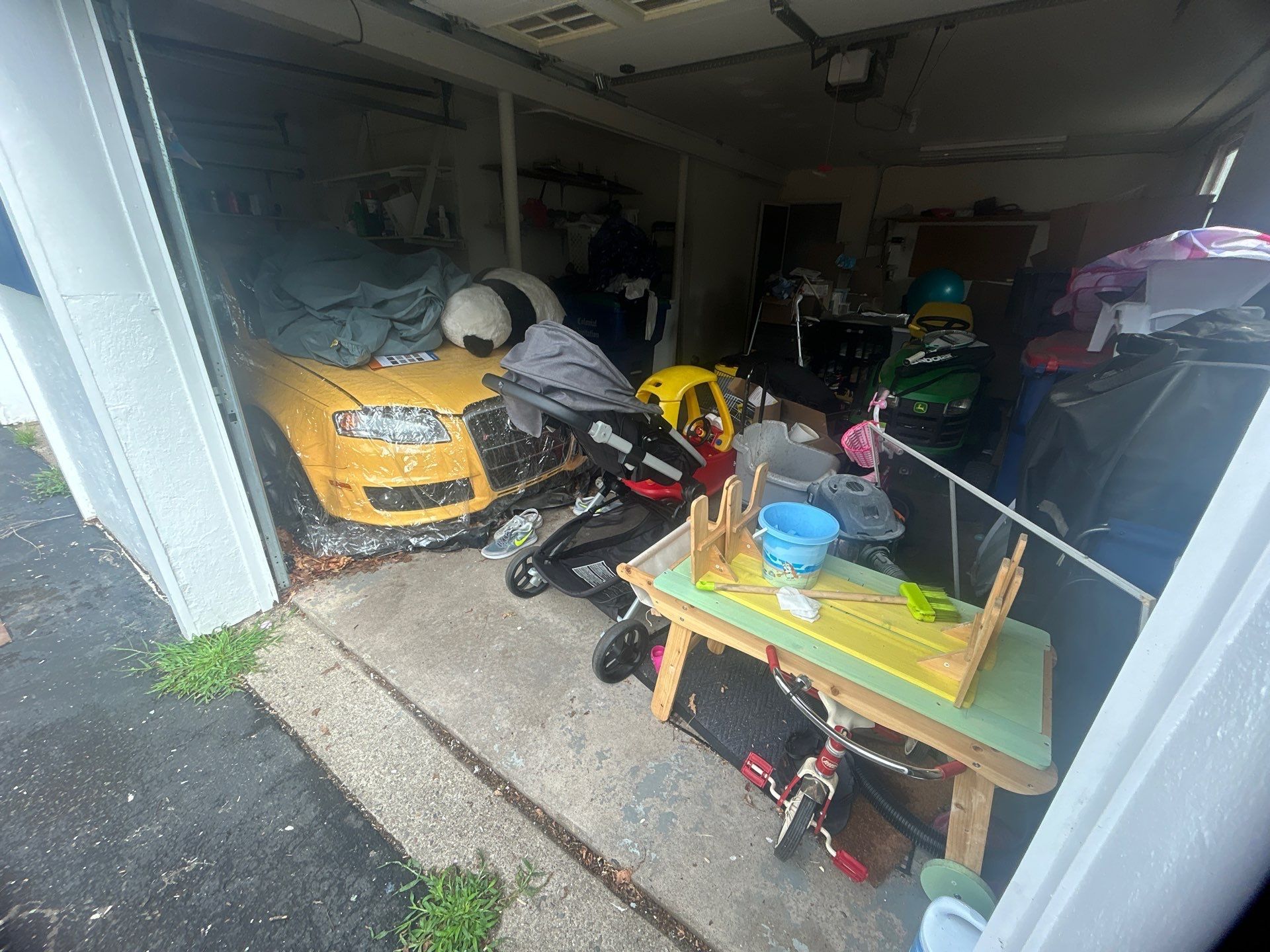 Cluttered garage with yellow car, toys, and a small table.