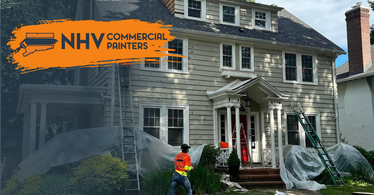 A person in a safety vest prepares to paint a multi-story house covered in drop cloths, with an NHV Commercial Painters logo.