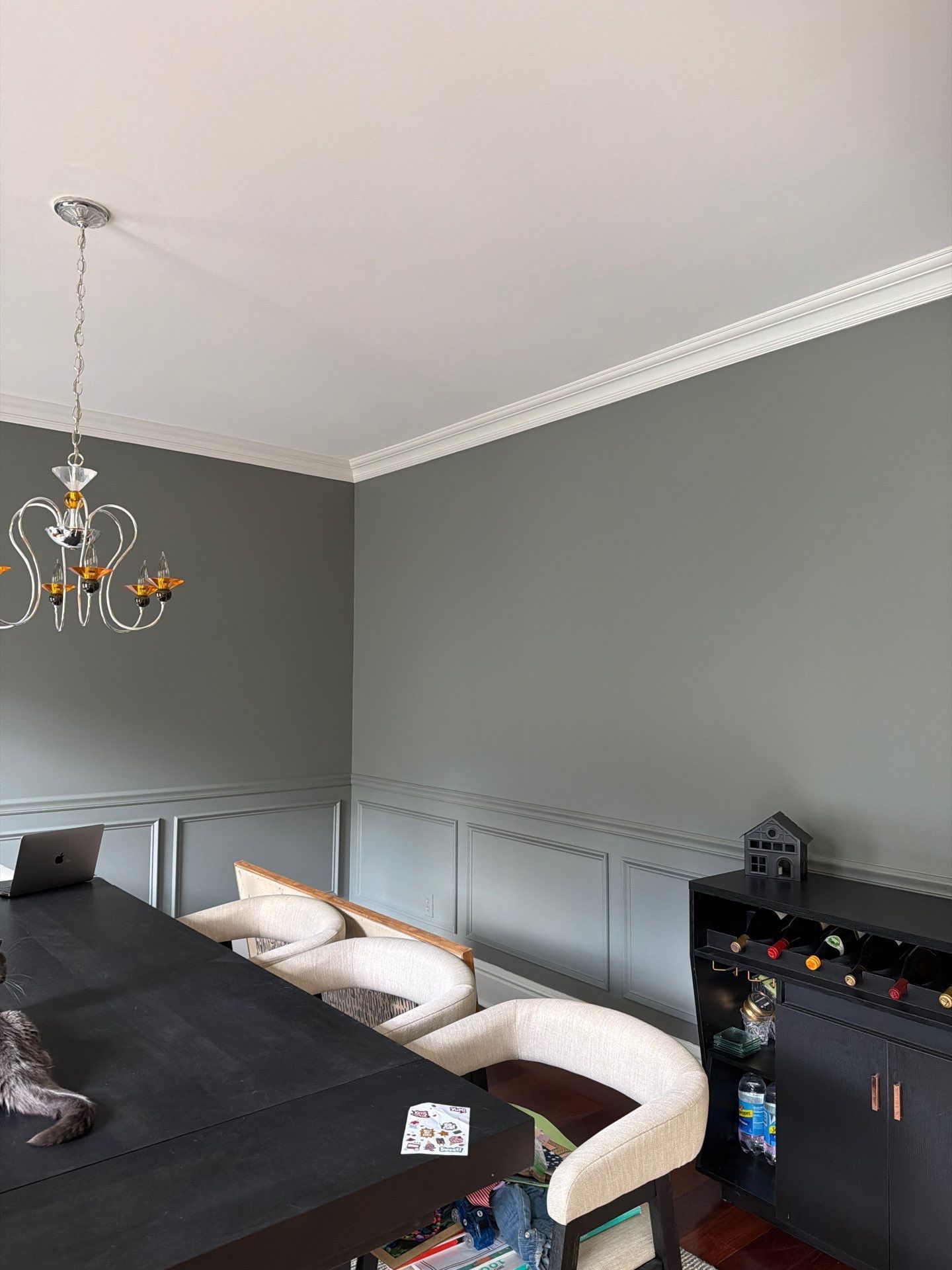 Dining room with gray walls, white crown molding, black table, and a chandelier.