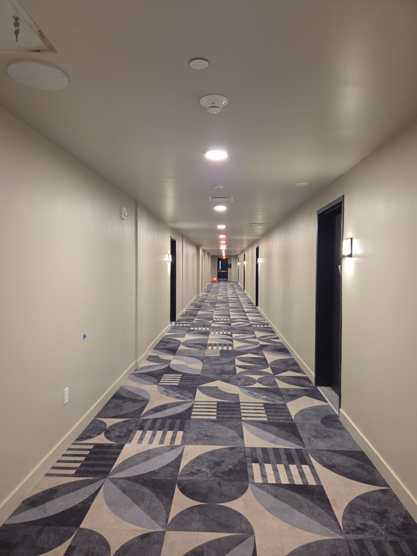 Long, carpeted hotel hallway with doors on either side and recessed lighting.