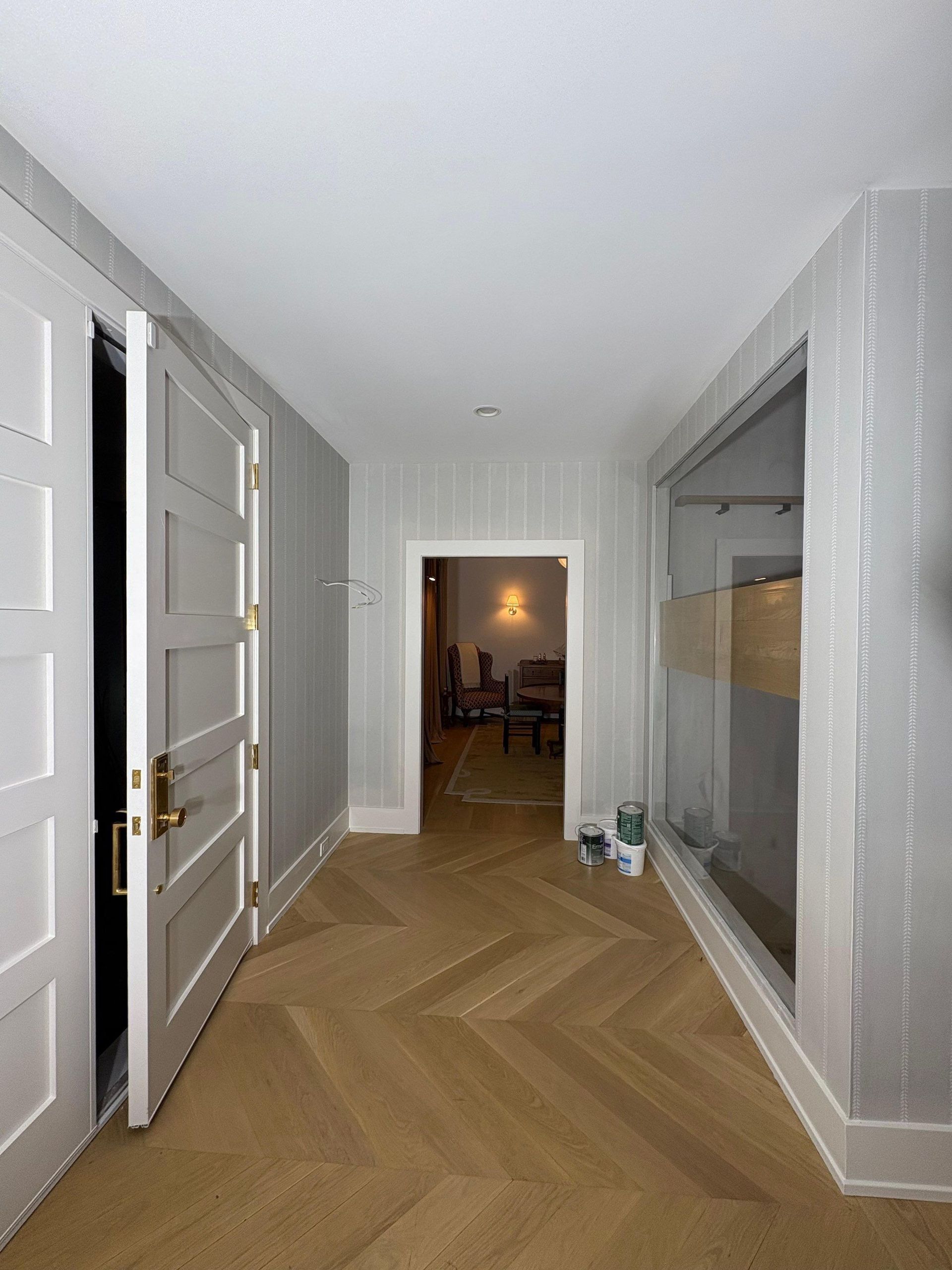 Hallway with gray walls, light wooden chevron floor, two white doors, and a glass-walled shower area.
