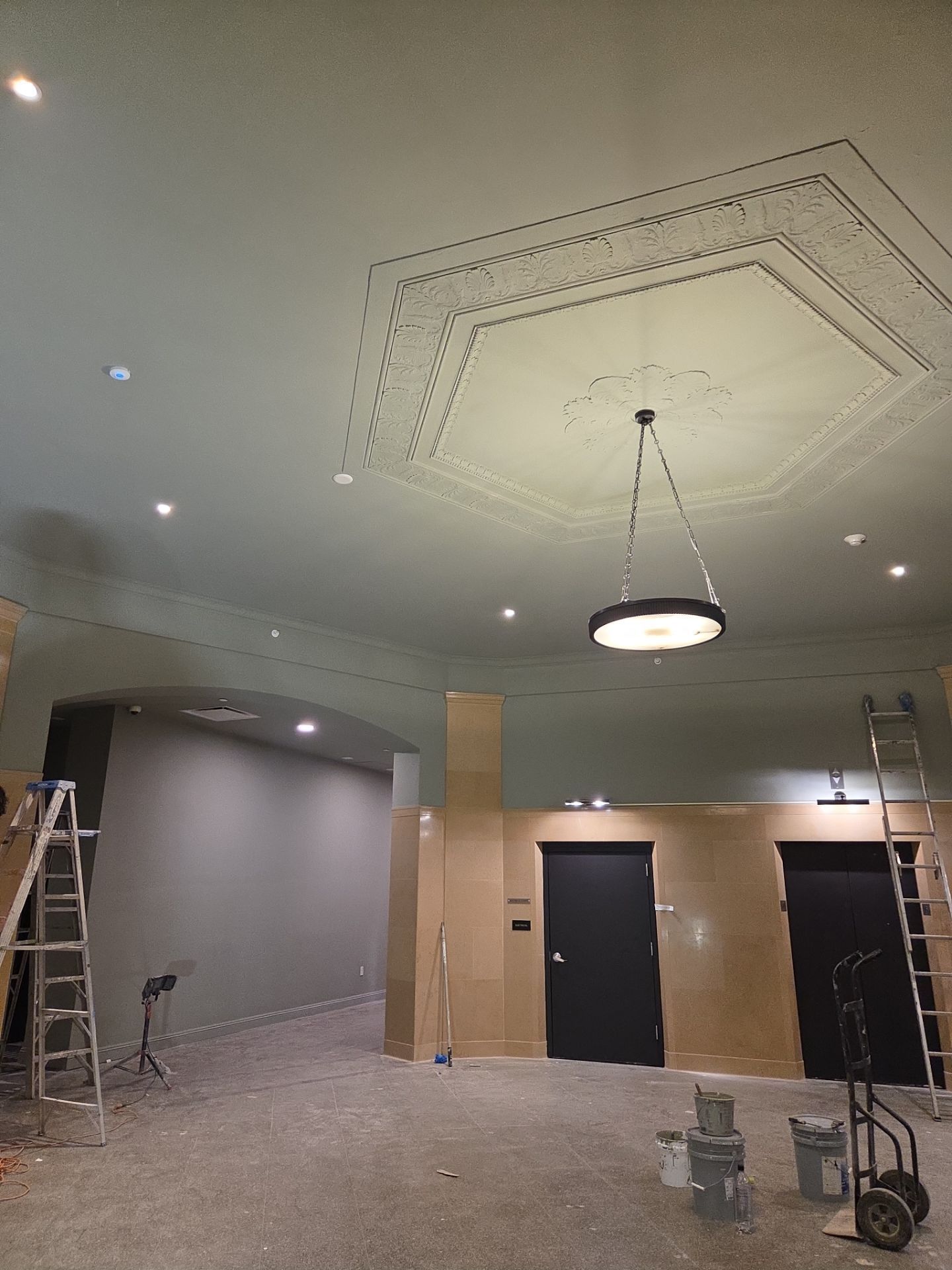 A room with pale green ceiling and ornate design, black doors, and construction equipment.