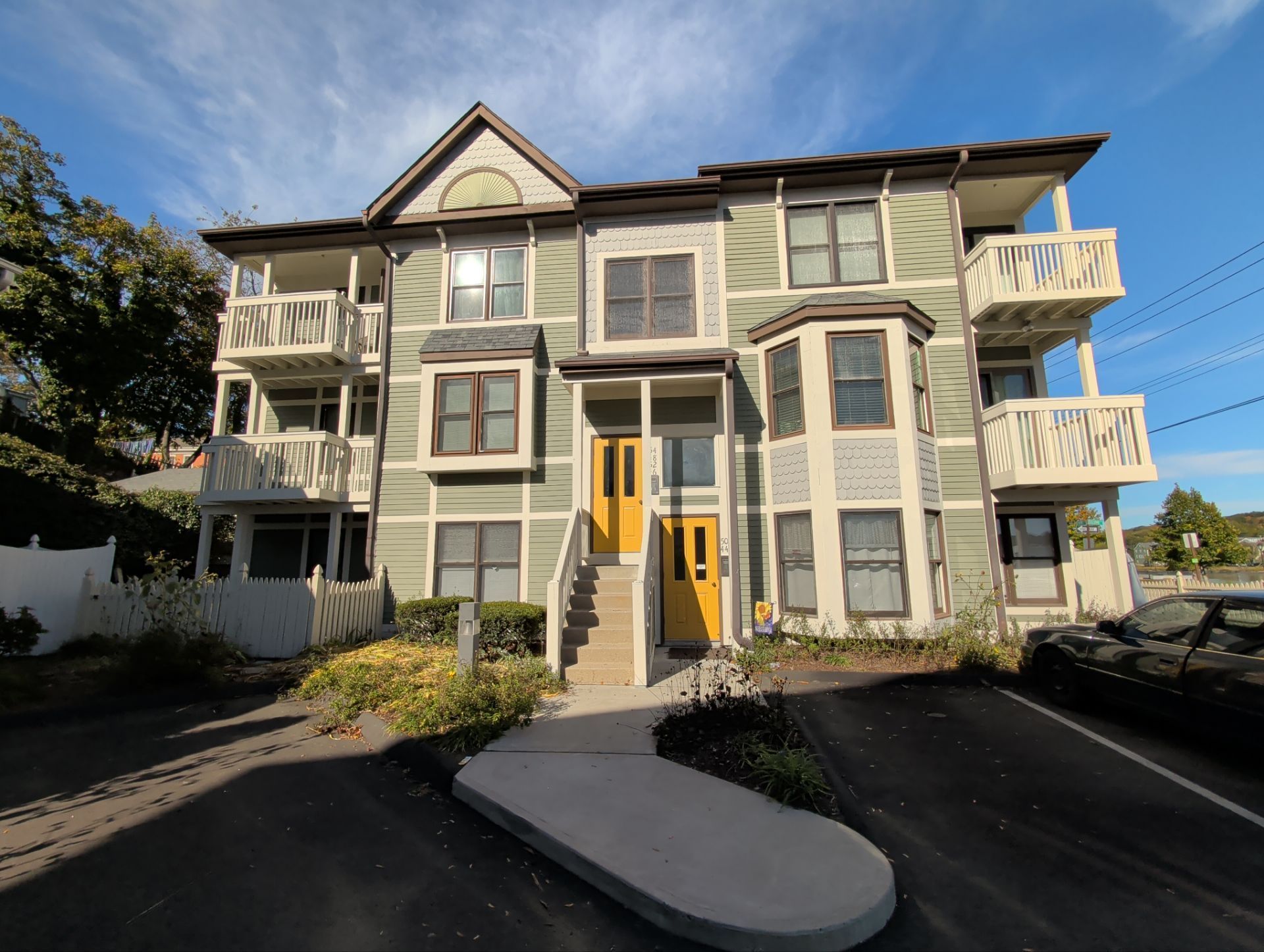 Three-story green building with yellow doors, balconies, and brown roof under blue sky.