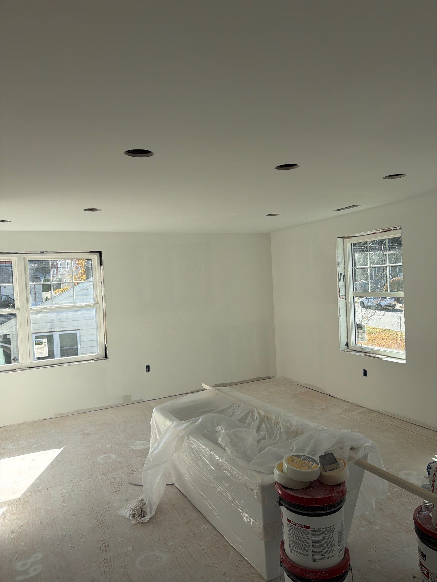 Empty room, freshly painted white. Bathtub covered in plastic. Construction site.