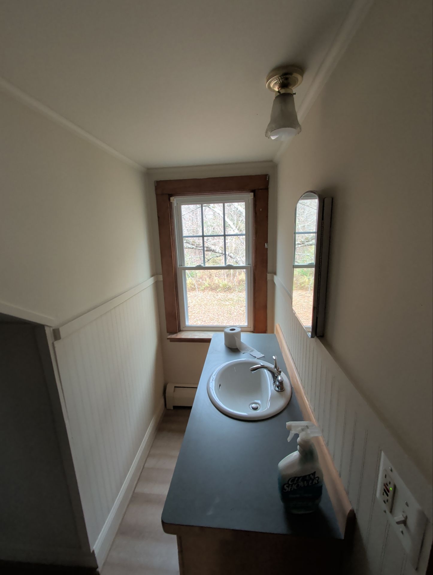 Small bathroom with sink, window, mirror, and light fixture. White walls, wood trim, dark countertop.