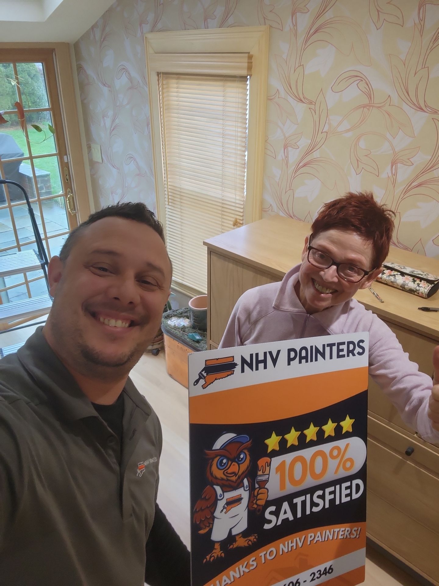 Two people smiling, holding a sign for NHV Painters: 