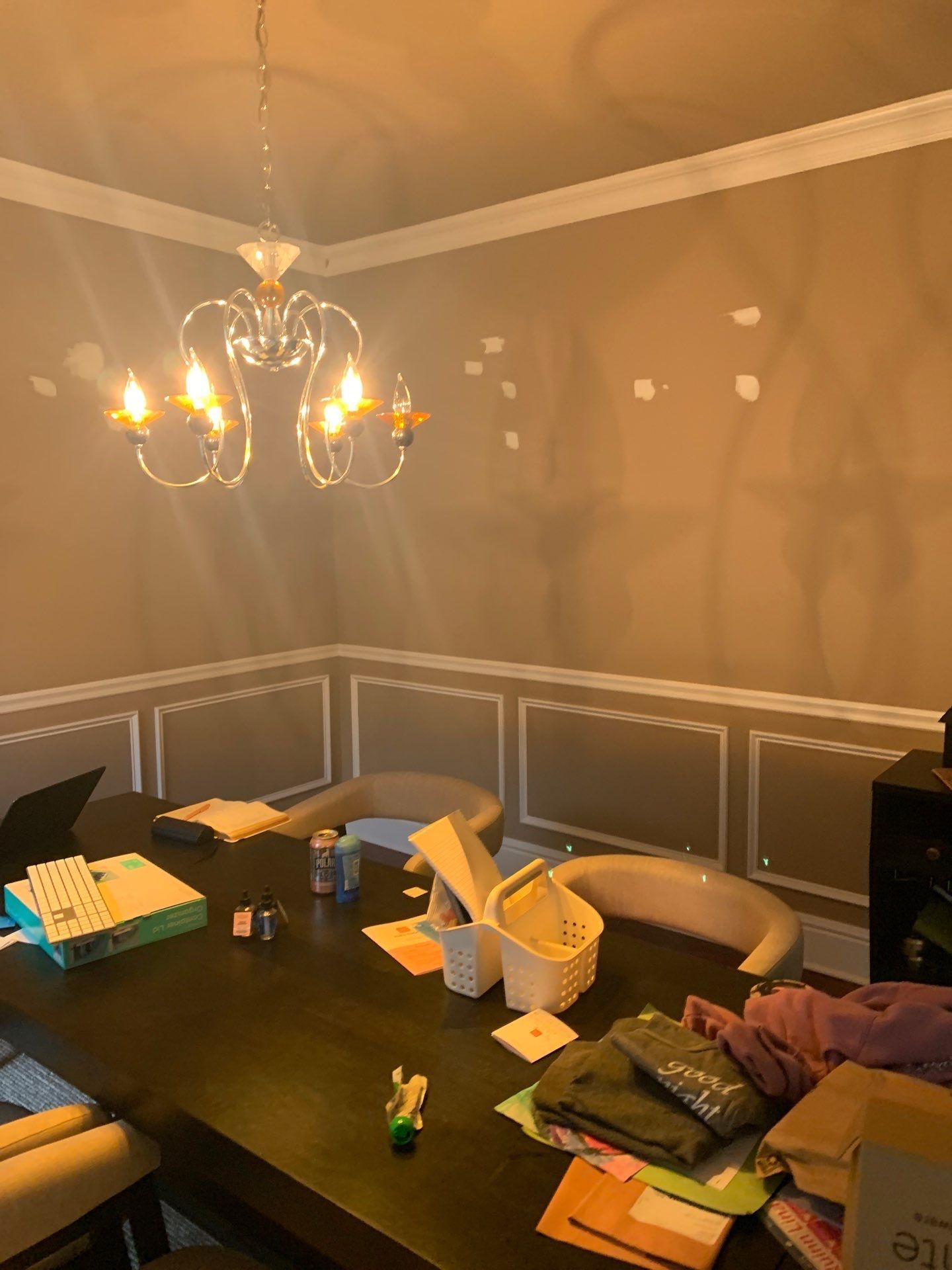 Dining room with chandelier, dark table covered with items, white trim, brown walls.