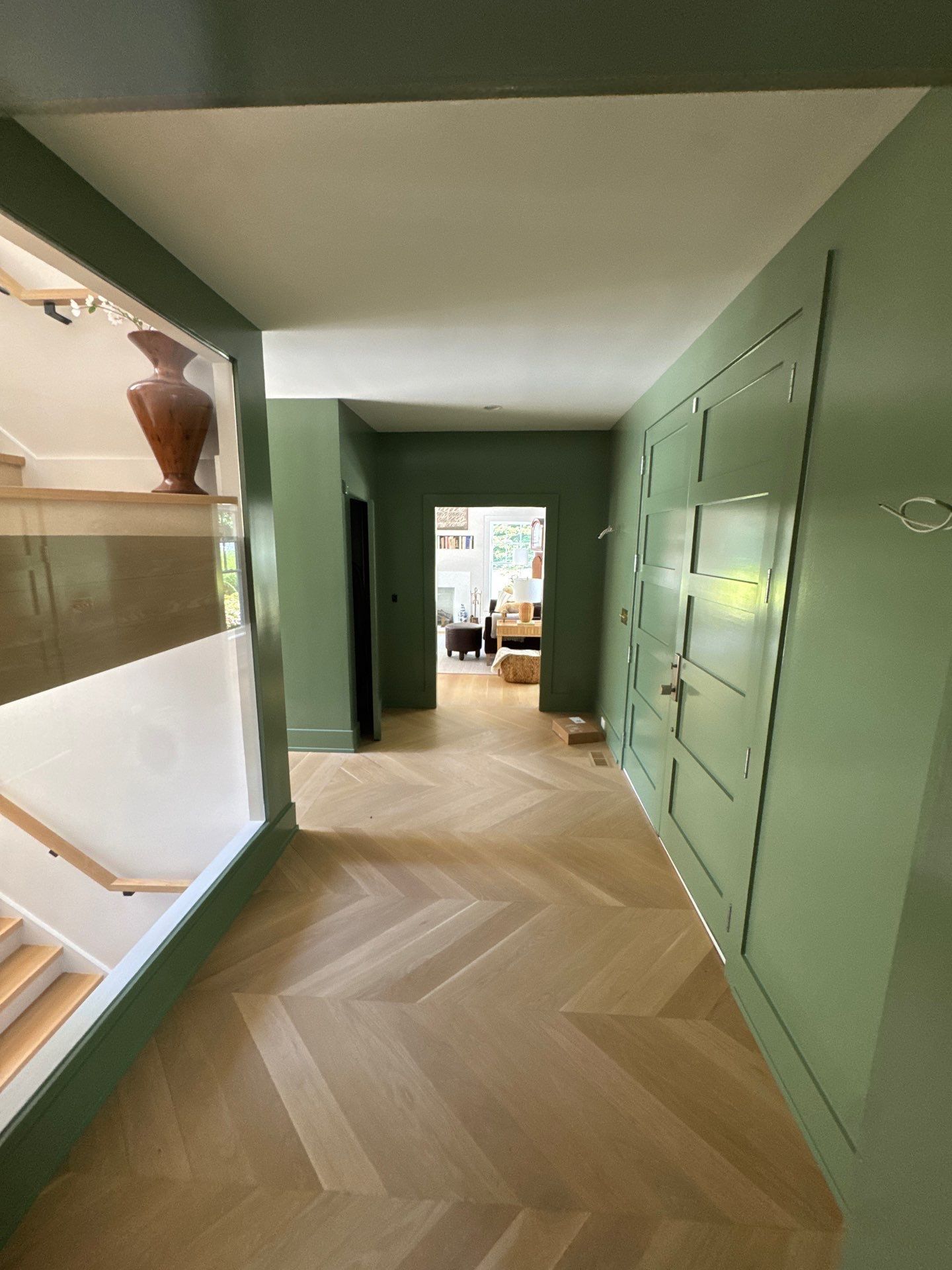 Hallway with light wood herringbone floors, green walls, and white ceiling.