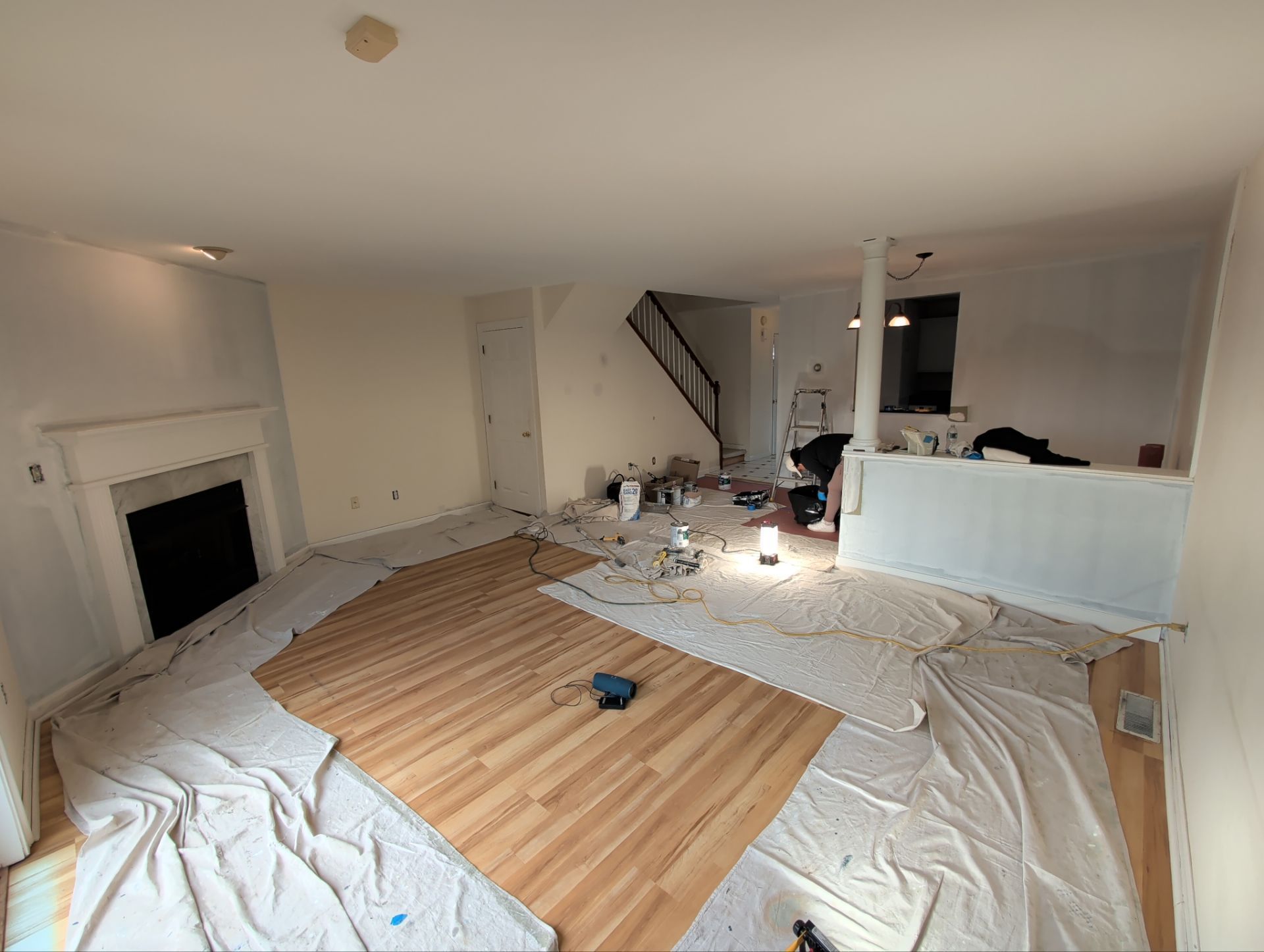 Room renovation in progress; hardwood floor being installed. Tarps, tools, and fireplace visible.