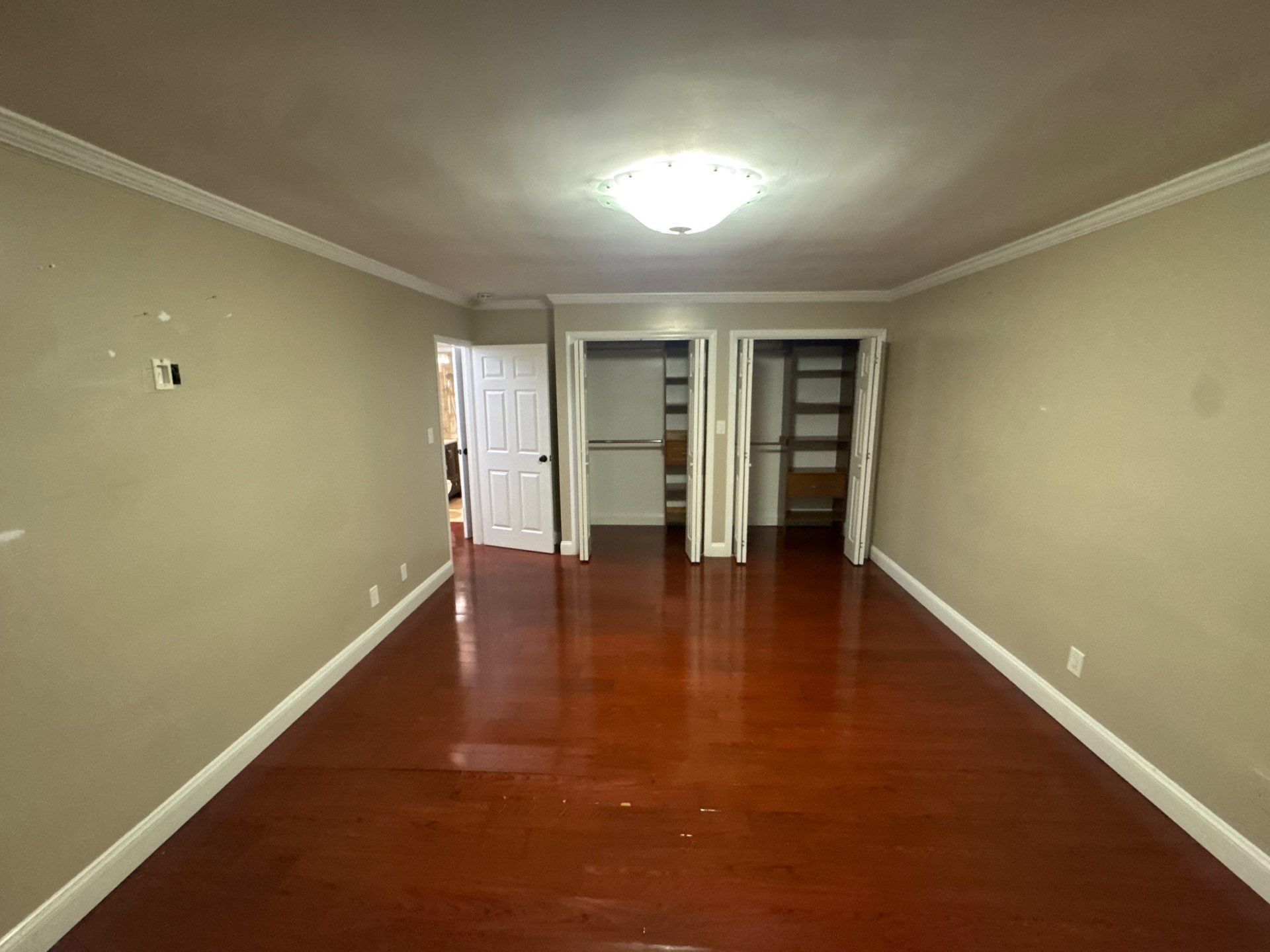 Empty room with dark wood floor, tan walls, and two closets. White trim and ceiling light.