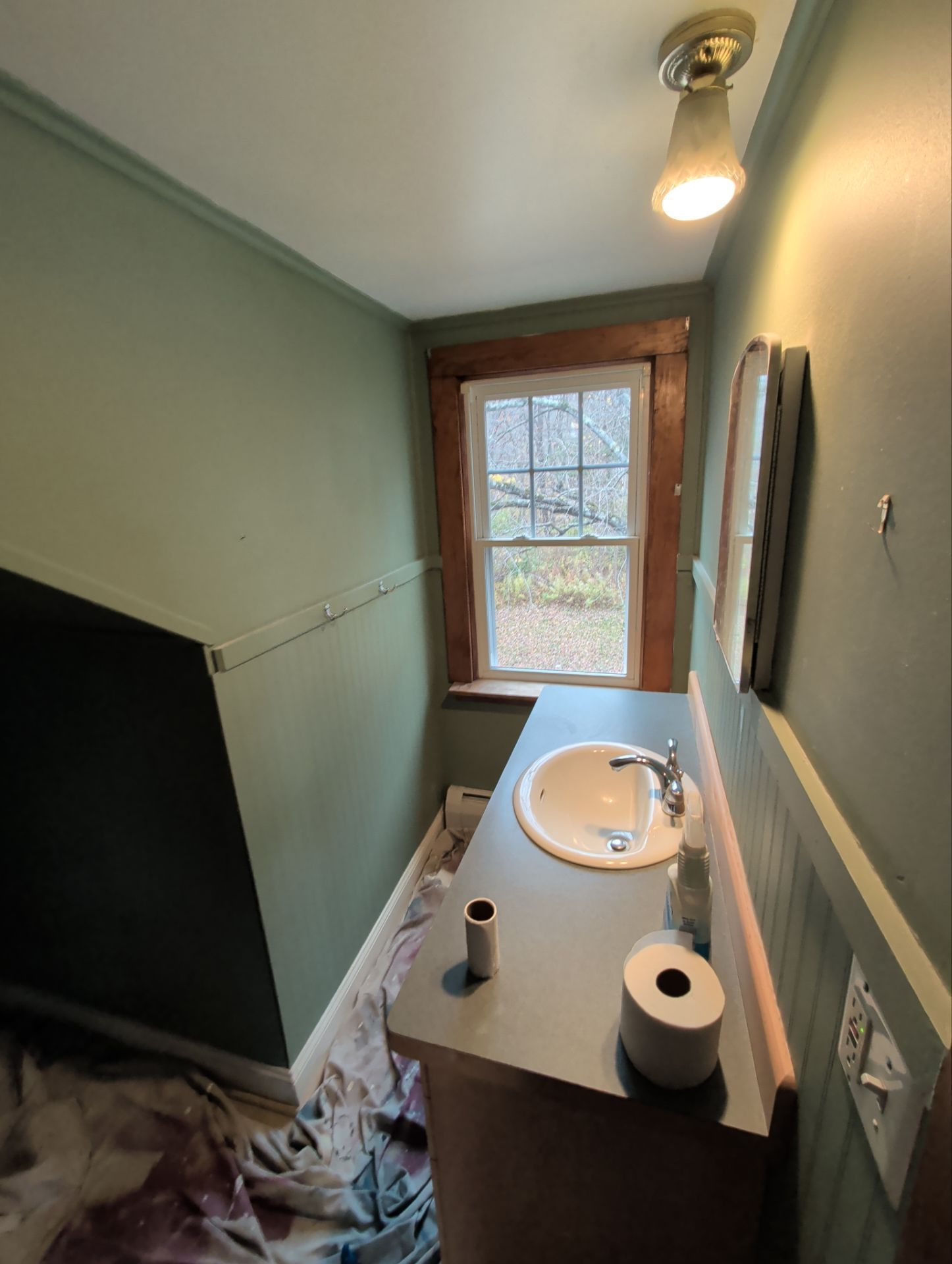 Small bathroom with a sink, mirror, and window; walls are green.