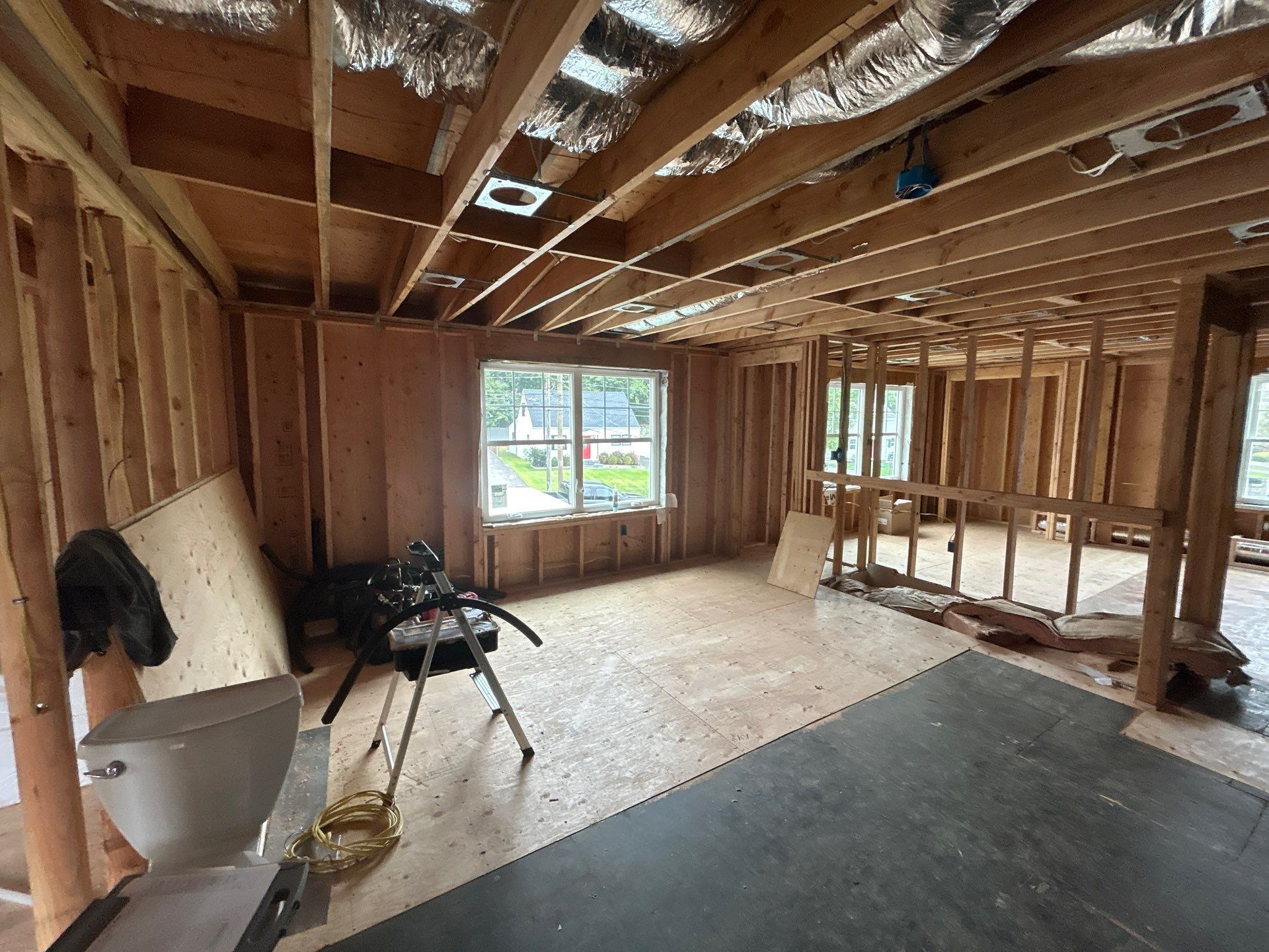 Interior of a house under construction; wooden frame, exposed beams, unfinished floors, and window.